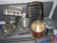 Photo displaying various kitchen cookware items including tin baking pans, large metal strainers, a copper pot, and the Mirro pressure cooker with lid.