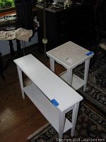 Two white painted wooden side tables, one narrow with lower shelf and one square with lower shelf, both lightly used.