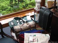 Photo showing multiple wine bottle carriers on a table near window, including dark green insulated wine picnic kit and brown map design carrier, plus fabric wine bags and themed towels.