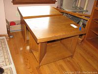 Two medium brown wooden end tables with open lower shelves, placed on a hardwood floor. Tables measure approximately 28"x22"x22.5". Visible scratches and wear noted on surfaces.