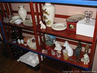Wide view of shelving unit with porcelain vases, dog and cat figurines, decorative plates, and small glass and porcelain items.