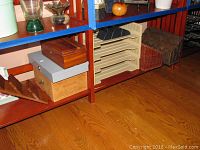 Wide view of lower shelf showing various boxes, letter holders, and paper organizer on wooden floor.