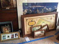 Various framed artworks displayed leaning against furniture and on floor; includes hunting scenes, map, mountain photograph, smaller portrait and collage frames.