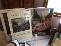 Three large framed posters leaning against wall, including Ansel Adams and Canadian Pacific Rail travel poster