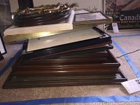 Stack of various picture frames in rectangular shapes, composed of wood, metal and plastic, showing side and front edges clearly indicating sizes between 5x7 through 18x20 inches.