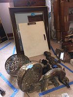 Photo showing wood framed mirror, plastic lap desk, pair of brass-look plant holders, brass horse sculpture, and brass dragon brackets on carpet