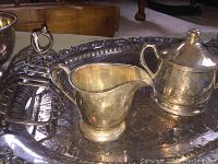Silver plated cream pitcher, lidded sugar bowl, and toast rack displayed on tray, showing signs of tarnish and use.