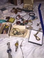 Overview of costume jewelry lot with bracelets, necklaces, pins, earrings, and watches on white fabric.