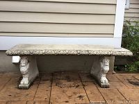 Full view of rectangular concrete garden bench with decorative lion head legs, placed on outdoor flooring.