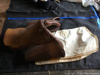 Photo of brown English leather riding saddle resting on beige canvas liner on ground.