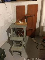 Photo of vintage wooden step stool and two long wooden shelves leaning against a basement wall.