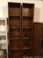 Full view showing two tall identical wooden bookcases side by side with five shelves each in a basement setting.