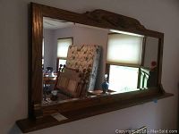 Full view of the wooden wall mirror showing the shelf and ornate carved top.