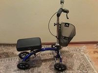 Single image showing a blue KneeRover deluxe steerable knee walker with padded knee rest and front basket. Four wheels and brake lever visible.