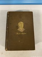 Front cover showing gilt portrait and author name, cloth wear and scuffs