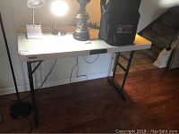 Full view of folding table set up indoors on wooden floor showing white plastic top, metal legs and surroundings.
