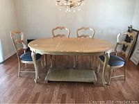 Dining table and four chairs arranged around it in a room with hardwood floor, showing table shape and style.
