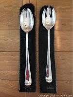 Pair of Gerity Modern American silver serving utensils, one spoon and one fork, each about 13 inches long resting on wood floor over black felt protective pouches.