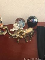 Photo shows four items: Selkirk glass orb with butterfly flower design, Correia glass orb with purple and black colors and butterfly motif, Lenox brass elephant figurine with trunk raised, and a small Lenox porcelain grasshopper figurine.