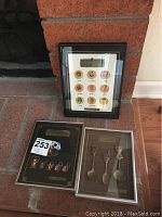 Photo showing three framed Seoul 1988 Olympic commemorative decor items placed on a brick floor near a fireplace. Includes Olympic pins and spoon sets.