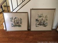 Pair of framed needlepoint artworks resting against a wall on a wooden floor, showing the full view of both pieces.