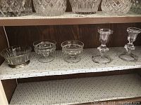 Shelf with three small crystal dishes and two hexagonal candle holders.