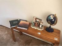 View of a wooden table with ceramic peddler figurine, globe, and three coffee table books on top