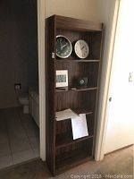 Full view of laminate bookshelf in interior setting showing five shelves containing few objects and the bathroom in background.