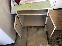 Small white storage cabinet with doors open, showing interior shelf and caster wheels.