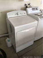 Front view of white Kenmore electric dryer with control panel and door handle visible, placed in a laundry area next to a washer.