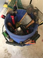 Photo of blue carry tote bucket filled with hand tools including hammers, screwdrivers, spray can, and wood handled tools.
