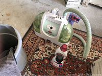 Bissell Little Green Machine portable cleaner with hose attachment and two small solution bottles.