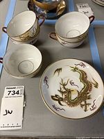 Three cups and one saucer showing dragon design and gold trim