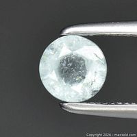 Round light bluish green faceted tourmaline held in tweezers