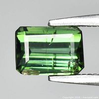 Rectangular octagon-cut green tourmaline held in tweezers showing clarity, colour and faceting