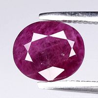 Front view of loose oval faceted ruby held by tweezers