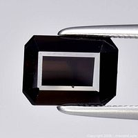 Octagon-cut deep yellow tourmaline held in tweezers showing facets and color