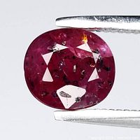 Front view of cushion-cut purplish red ruby held by tweezers showing overall color and faceting