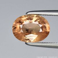 Close-up of oval faceted yellow zircon gemstone held by tweezers
