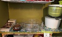 Shelf showing clear divided tray, salad spinners stacked, coasters on left