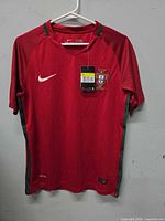 Front view of red Nike Portugal jersey on hanger showing crest and tags