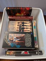 Top view of basket containing VHS tapes showing Volcano, Atlantic Vistas, The Craft, Flashdance, Bambi, Spy Kids 2 cases