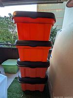 Four orange storage totes stacked, showing black lids