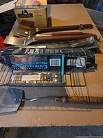 Lot showing three wood-handled stainless spatulas, GrillPro roasting basket, Olympian dust cover box