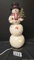 Front view of ceramic snowman lamp showing star cutouts and cord