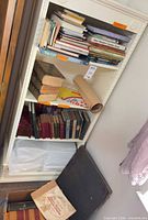 Full bookshelf view with assorted books, red set, rolled poster, portfolio on floor