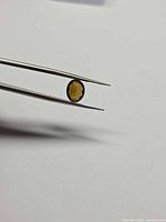 Oval cognac orange gemstone held in tweezers showing face-up view