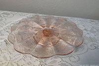 Top view of pink etched glass cake stand showing scalloped rim and etched pattern