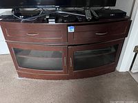 Front view of dark brown curved TV stand showing drawers and glass doors