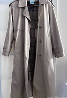 Front view of beige London Fog trench coat showing length, double-breasted style, epaulettes, storm flap, plaid lining
